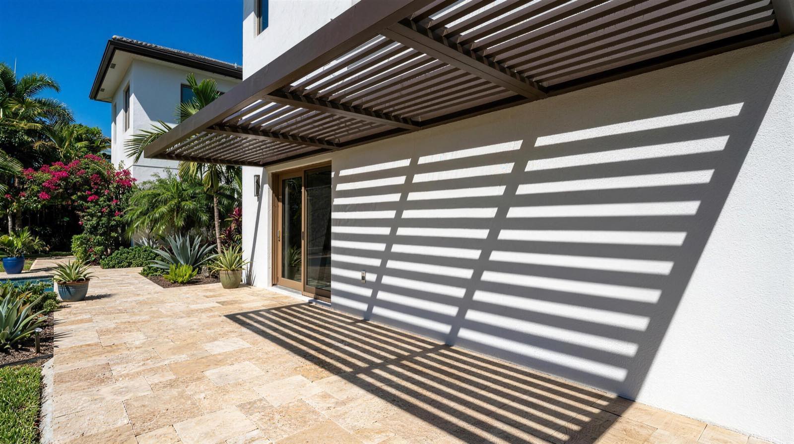 Hard-edged shadow stripes cast by an aluminum slat awning across a paver patio in bright afternoon sun
